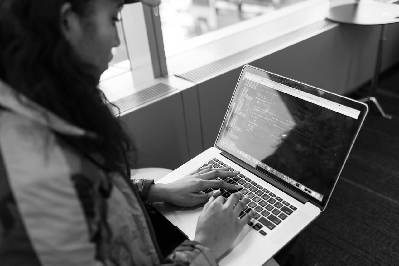 A woman typing code on a laptop in a modern indoor setting, showcasing tech work.